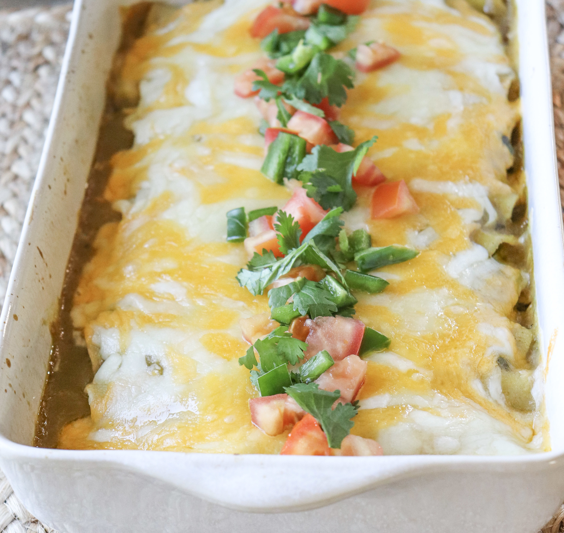 a casserole dish or prepared green chili chicken enchiladas garnished with jalapeno, cilantro and Roma tomatoes