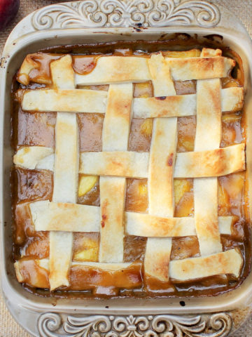 baking dish of prepared peach cobbler with visible peach slices and a golden brown lattice pie crust