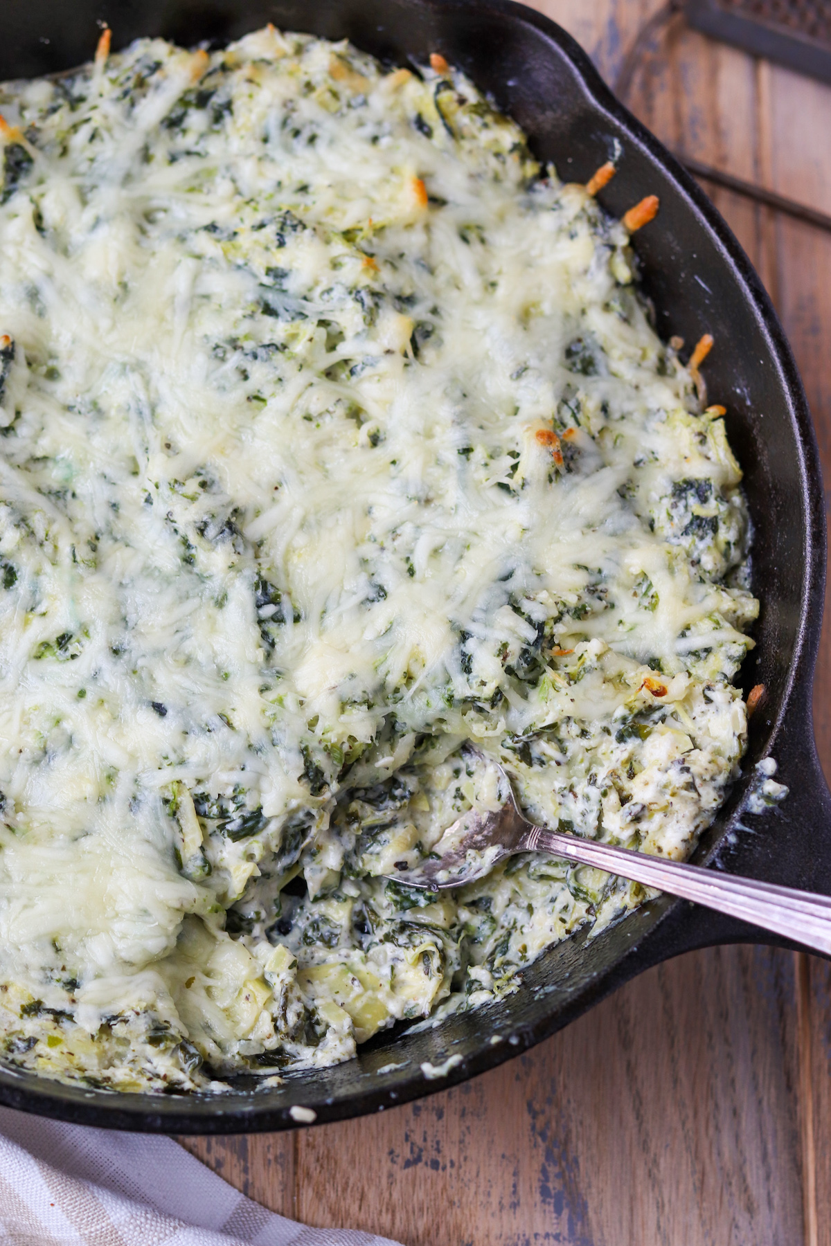 cast iron skillet with prepared spinach artichoke dip, melty cheese on top and creamy texture