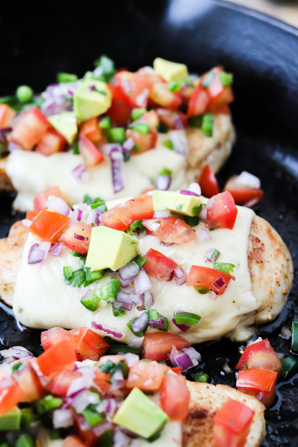 chicken breasts in a cast iron skillet with pepper jack cheese and a scoop of homemade pico de Gallo