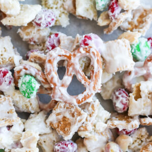 A close-up image of a white trash candy mix, consisting of golden grahams cereal, chex cereal, peanuts, m&m's, pretzels coated in melted white chocolate.