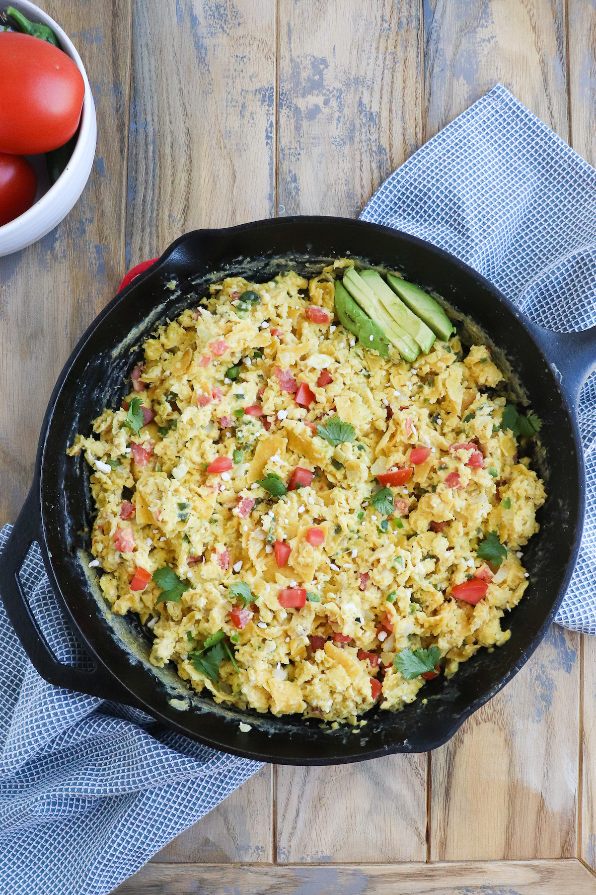 cast iron skillet of eggs scrambled with corn tortillas, tomatoes, and peppers