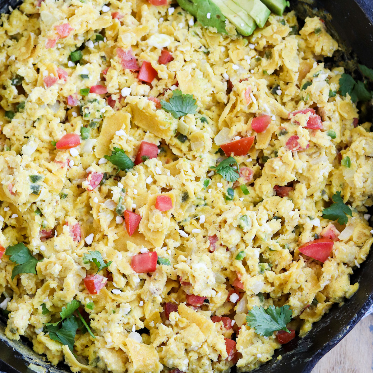 cast iron skillet of scrambled eggs with crispy tortilla strips, jalapeños, onions, tomatoes and topped with cheese