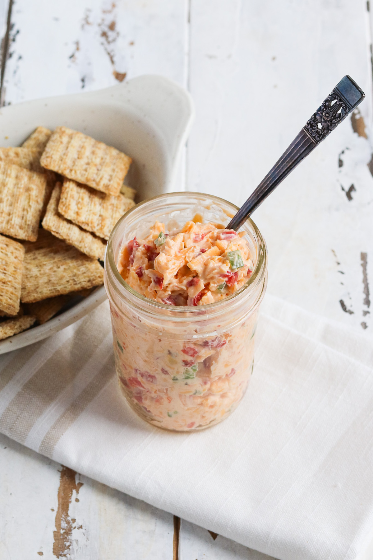 Plate of crackers and a jar of jalapeno pimento cheese spread with visible pieces of diced jalapenos and pimentos.