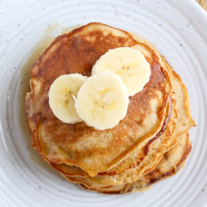 a short stack of prepared banana pancakes topped with three banana slices and syrup