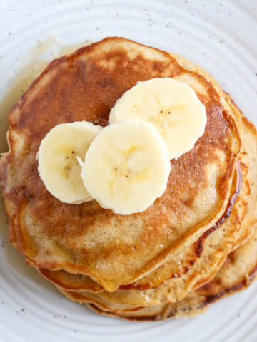 a short stack of prepared banana pancakes topped with three banana slices and syrup
