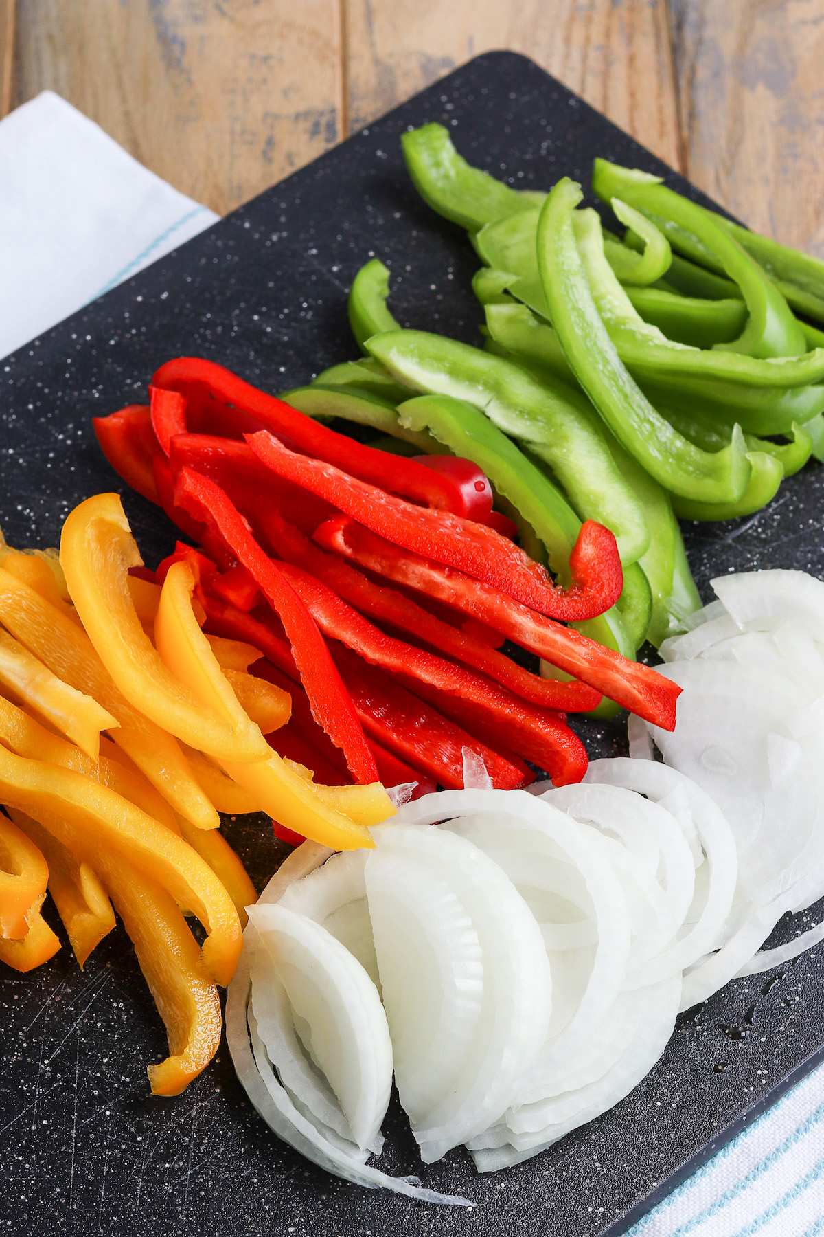 cutting board of sliced yellow, red, green bell pepper and white onion