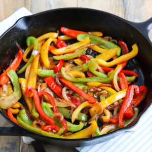 cast iron skillet of sautéed fajita bell peppers and onions. onions are slightly brown and peppers are charred.