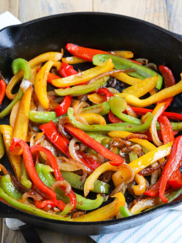 cast iron skillet of sautéed fajita bell peppers and onions. onions are slightly brown and peppers are charred.