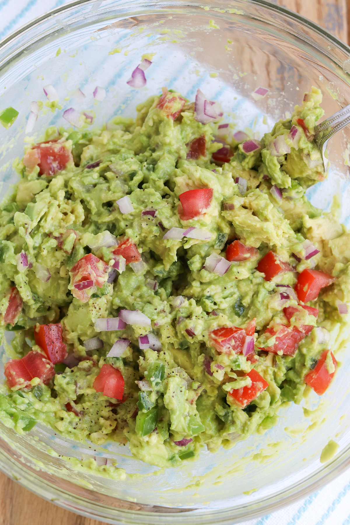 bowl of semi-mashed avocado with chunks of tomato and purple onion
