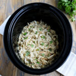 crockpot of prepared shredded chicken garnished with cilantro