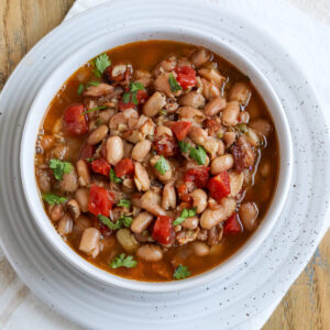 cooked charro beans in a bowl with visible chunks of tomato, bacon and top with cilantro