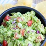 closeup of chunky guacamole in a bowl surrounded by tortilla chips
