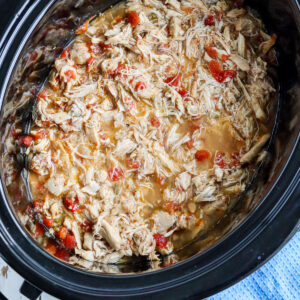 closeup of shredded cooked chicken in slow cooker with visible tomato pieces