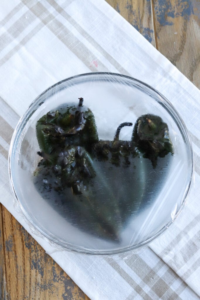 poblano peppers steaming in glass bowl with plastic cover