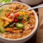bowl of white chicken chili with shredded chicken, beans, tomatoes and topped with tortilla strips avocado and jalapeno