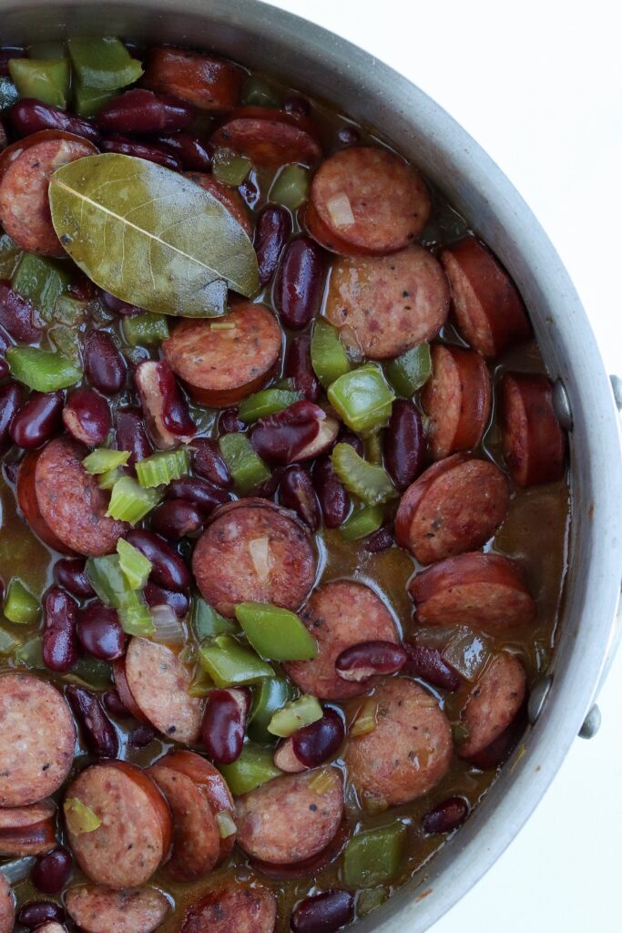 skillet of prepared canned cajun red beans with visible bay leaf and celery