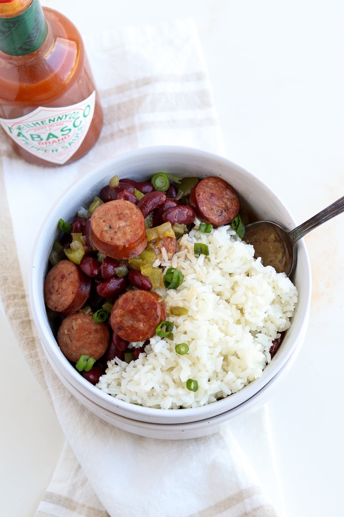 bowl of prepared red beans and rice garnished with green onion and tabasco sauce