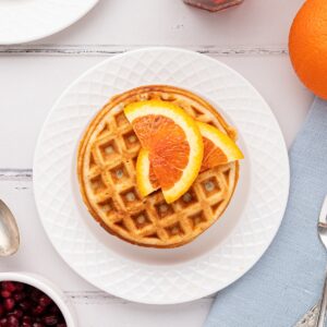 stack of prepared orange waffles on white plate with sliced oranges