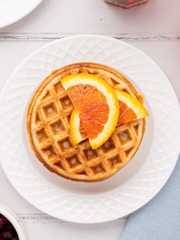 stack of prepared orange waffles on white plate with sliced oranges