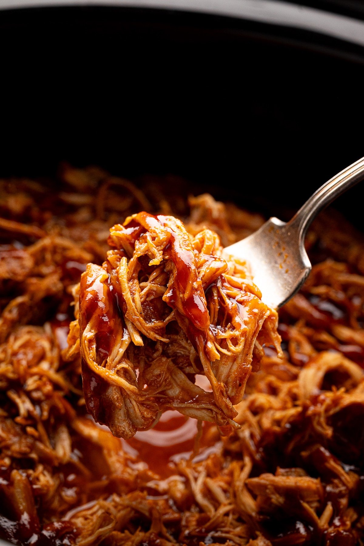 juicy flavorful shredded bbq chicken on a fork over slow cooker