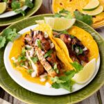 plated cilantro lime chicken tacos garnished with lime, cilantro and onion