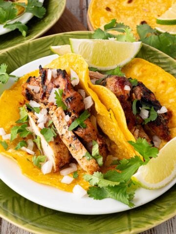 plated cilantro lime chicken tacos garnished with lime, cilantro and onion
