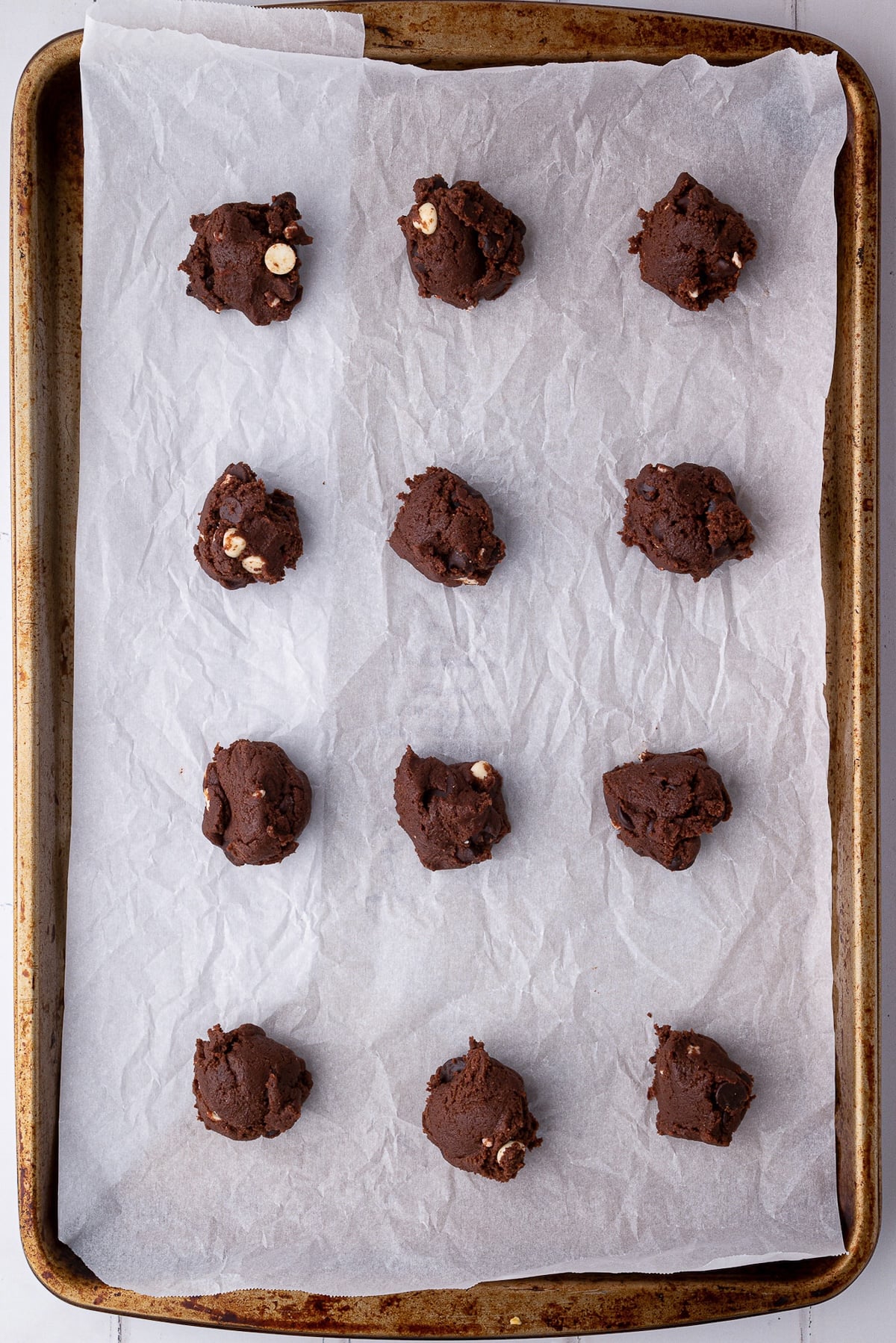 Scoops of thick chocolate cookie dough on a lined baking sheet.