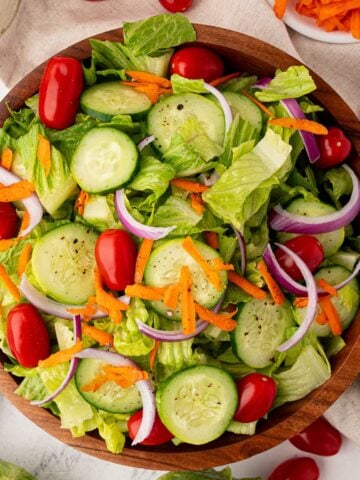 A bowl of the best house salad, with lettuce, tomatoes, carrots, red onion and ranch dressing.