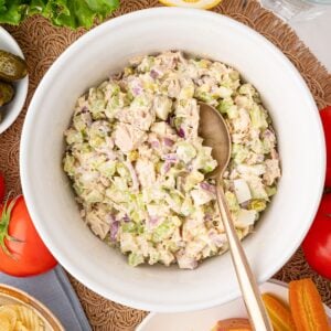 A bowl of mom's classic prepared tuna salad with flaked tuna, diced celery, dill pickles, red onion tossed with a little bit of mayonnaise. The bowl is surrounded by sandwich toppings.