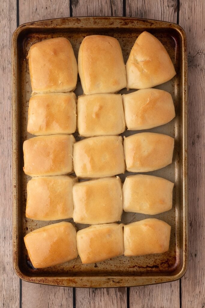 A baking sheet with 15 baked fluffy dinner rolls.