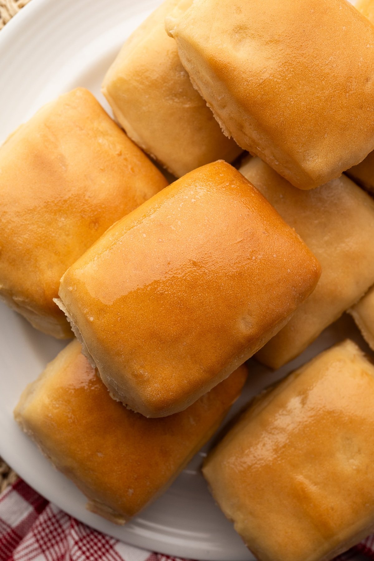 Pillowy, soft dinner rolls on a plate. The rolls are perfectly golden brown with a slight shine from being brushed with butter.