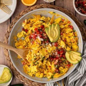 Tex-Mex style Migas featuring scrambled eggs, sautéed jalapeños, onions and tomatoes, fried corn tortilla strips garnished with pico de Gallo and avocado slices.