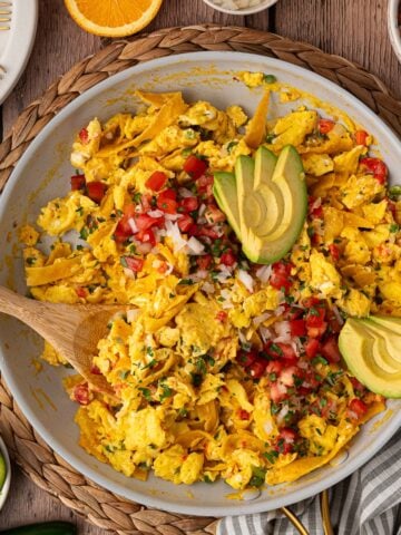 Tex-Mex style Migas featuring scrambled eggs, sautéed jalapeños, onions and tomatoes, fried corn tortilla strips garnished with pico de Gallo and avocado slices.