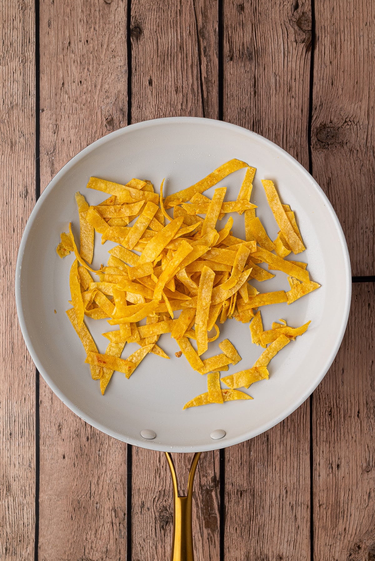 Frying corn tortilla strips till golden brown in skillet.