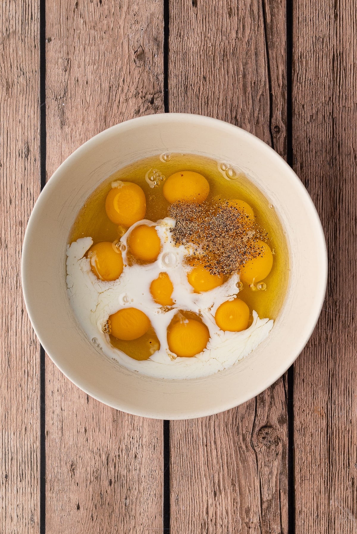 Mixing eggs with milk and spices in large mixing bowl.