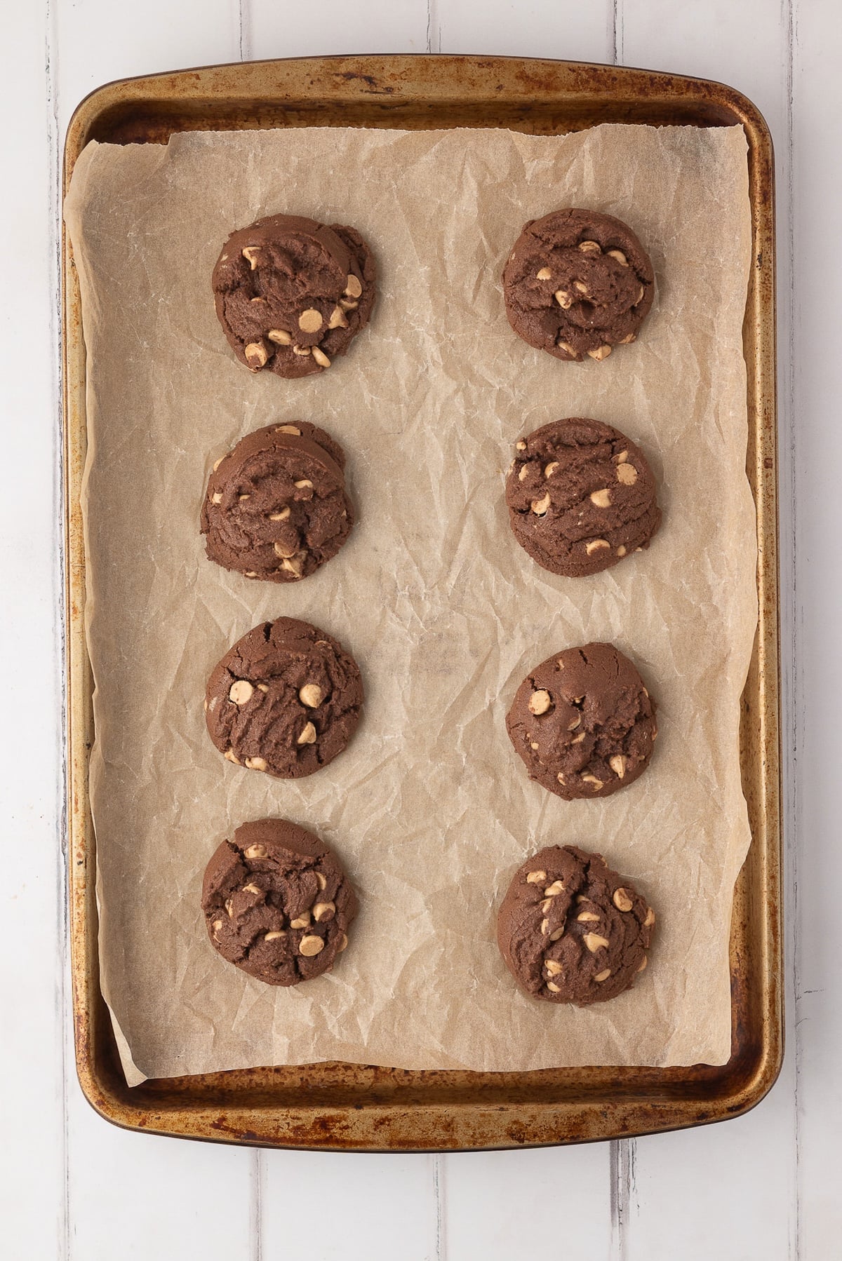 Freshly baked chocolate cookies with melted peanut butter chips cooling on baking sheet after just coming out of the oven.