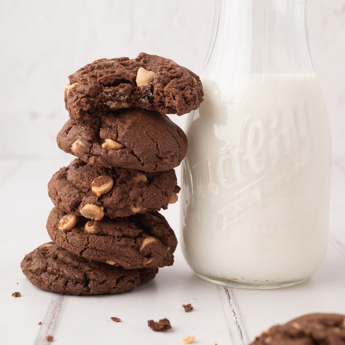 A tall, vertical stack of soft and chewy chocolate peanut butter chip cookies showing the rich cocoa texture and melted Reese's chips next to a vintage bottle filled with milk.