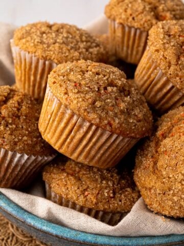 A bowl of freshly baked, healthy whole wheat carrot muffins with crunchy turbinado sugar tops, perfect for a Spring or Easter breakfast.