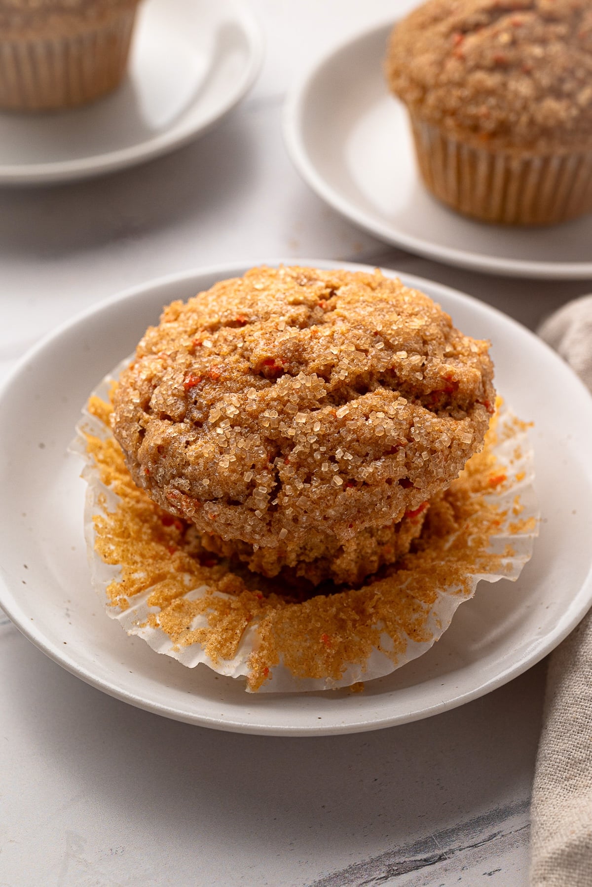 A golden-brown whole wheat carrot muffins with a crunchy turbinado sugar topping on a white breakfast plate.