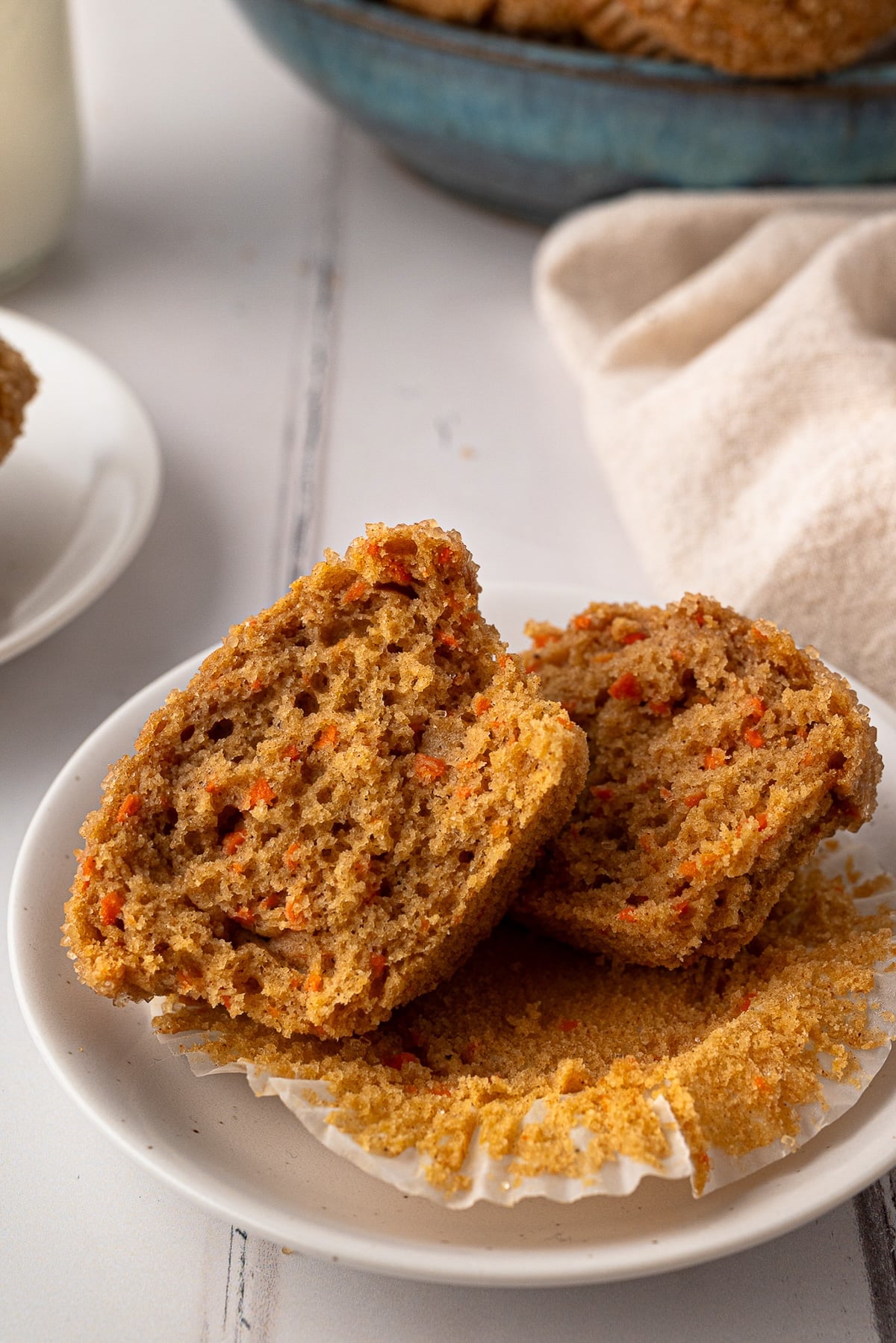 A whole wheat carrot muffin sliced in half on a white plate, revealing a moist, tender crumb filled with finely shredded fresh orange carrots.