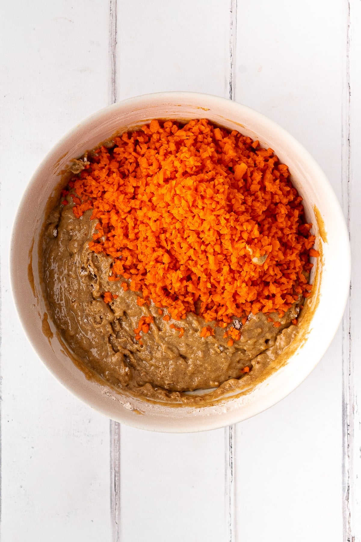 Folding bright orange shredded carrots into the whole wheat muffin batter.