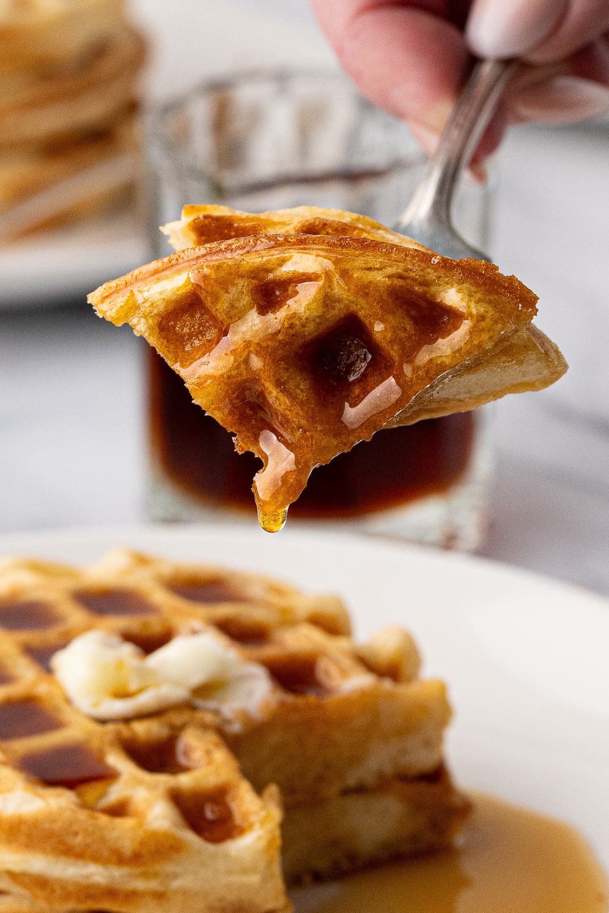 Macro shot of the crispy texture and deep pockets of the homemade buttermilk waffle with melting butter and syrup.