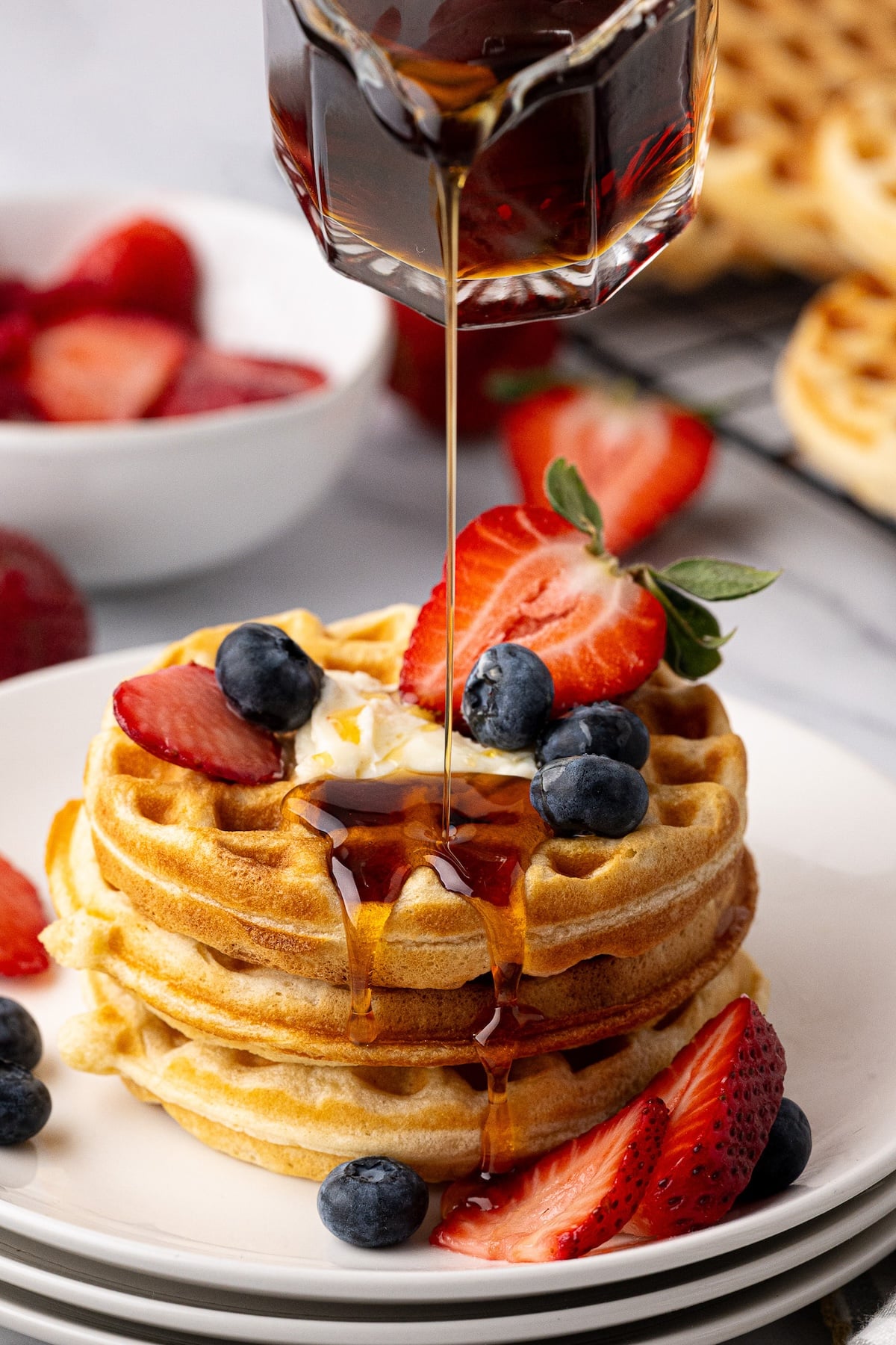 Pouring maple syrup onto a stack of the best homemade buttermilk waffles.