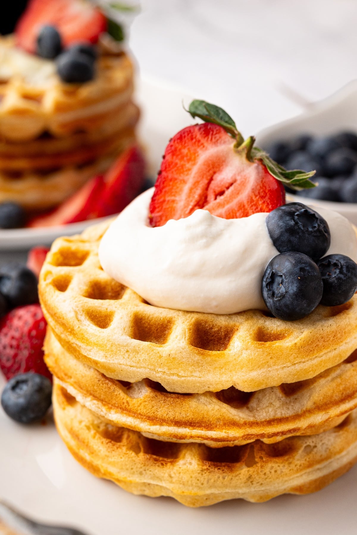 A tall stack of thick and fluffy buttermilk waffles toped with cream and fresh berries.