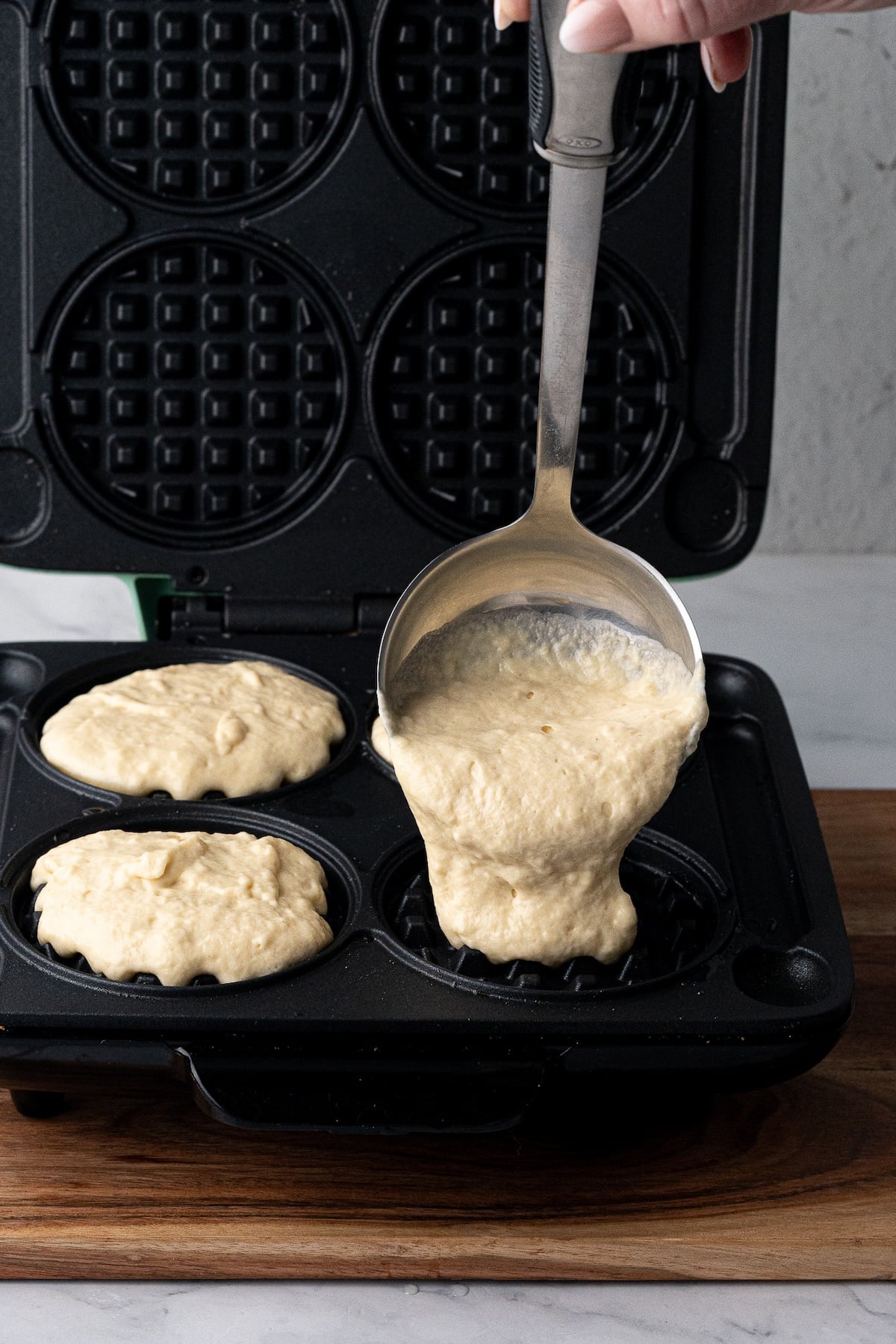 Pouring thick homemade waffle batter into a preheated waffle iron to cook.
