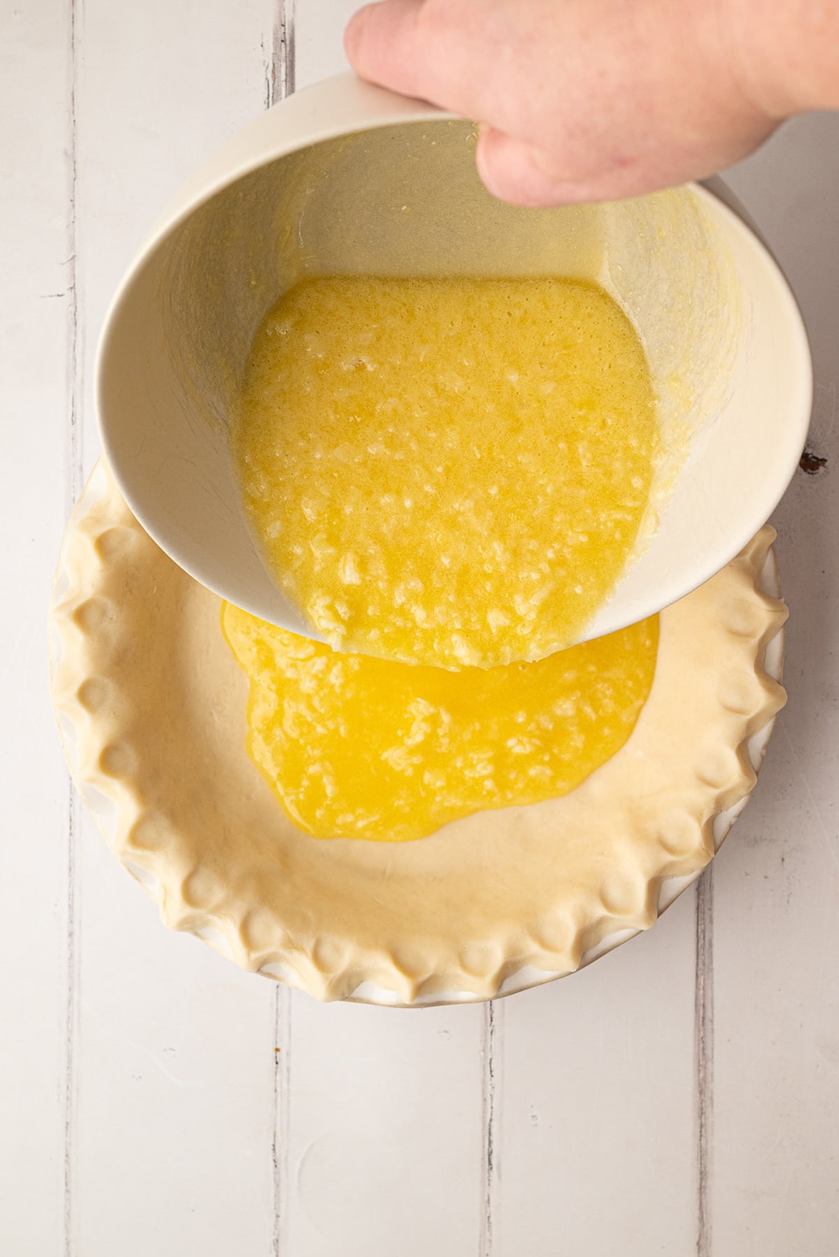 Pouring a smooth, whisked buttermilk and coconut pie filling directly into an unbaked pie crust before baking.