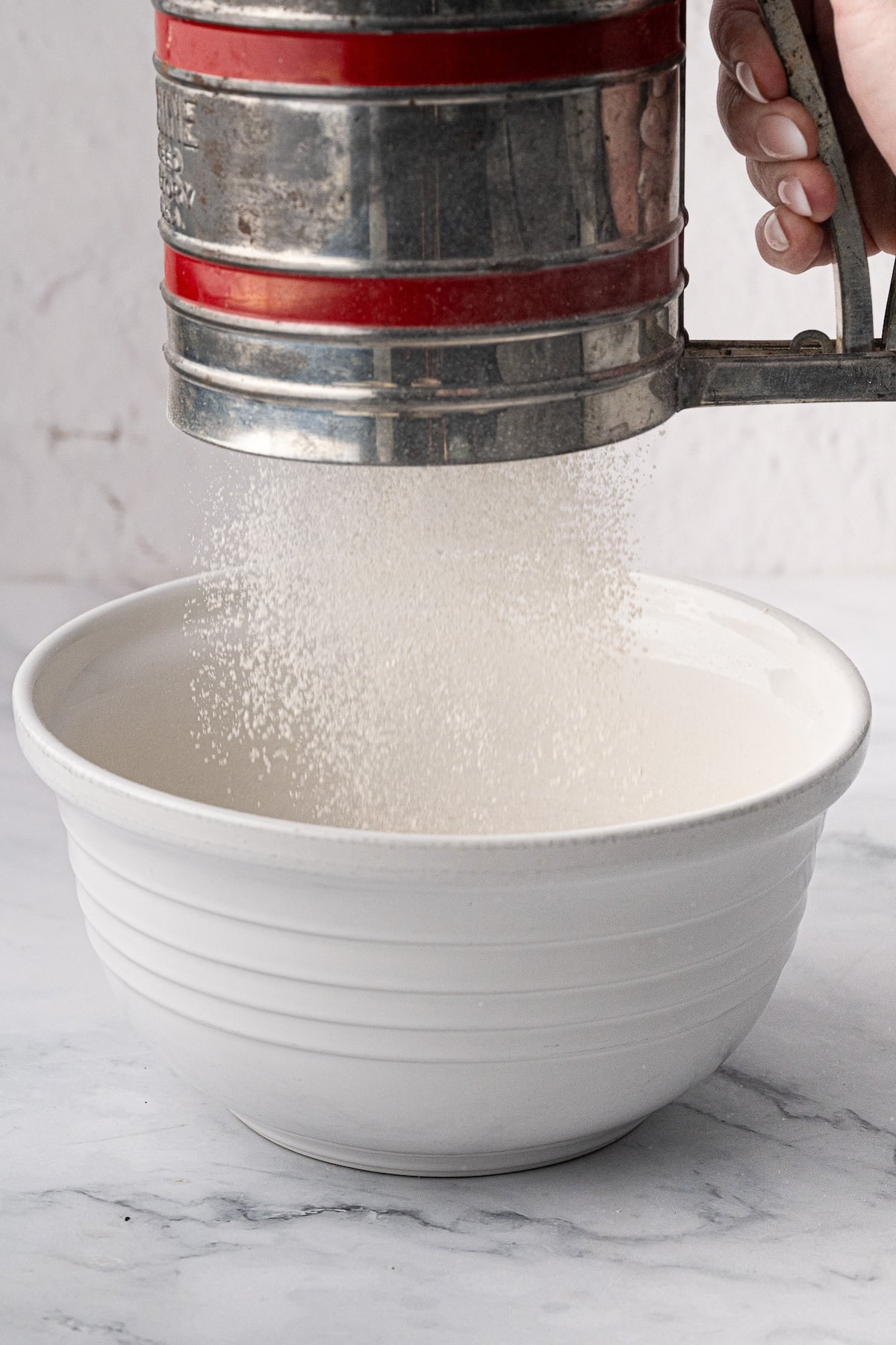 Sifting the dry ingredients together into a large ceramic mixing bowl for waffle batter.