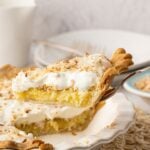 A side view of a slice of easy coconut pie lifted on a pie server, showcasing the baked custard-like pie filling and creamy whipped topping.