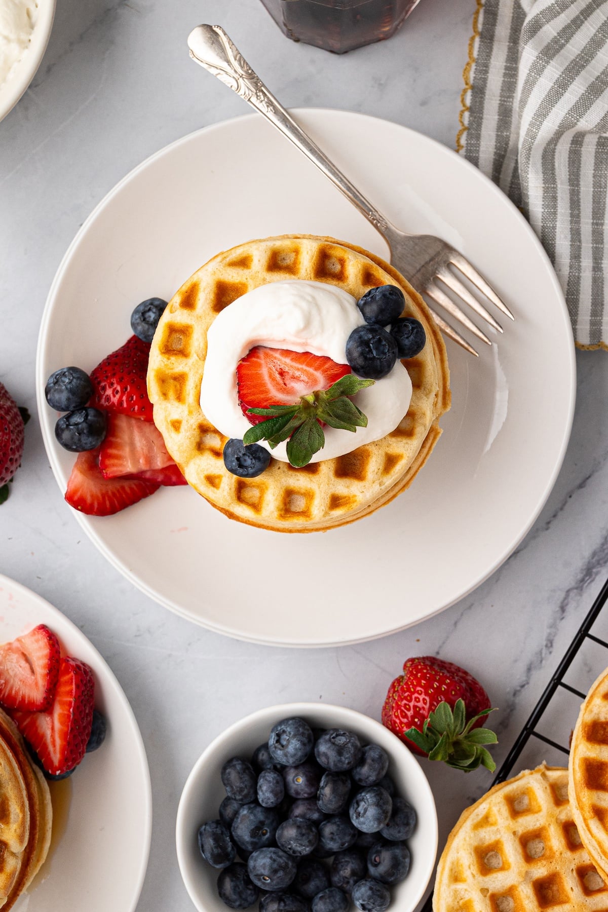 Golden brown buttermilk waffles on a white plate served with maple syrup, cream and fresh berries.